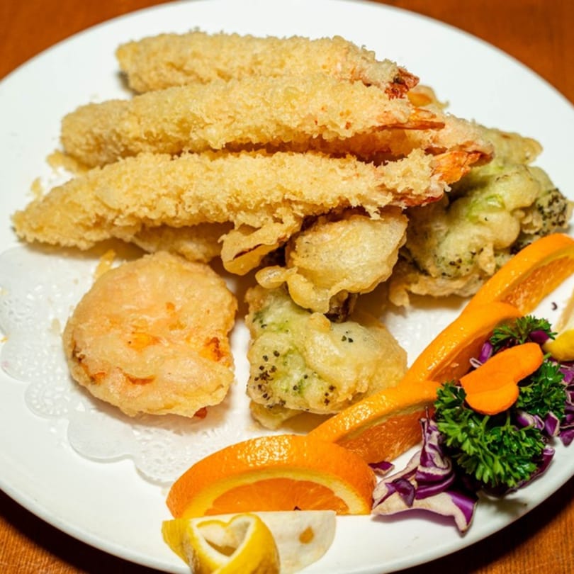Crispy tempura shrimp and vegetables, garnished with orange slices and parsley, on a white plate.