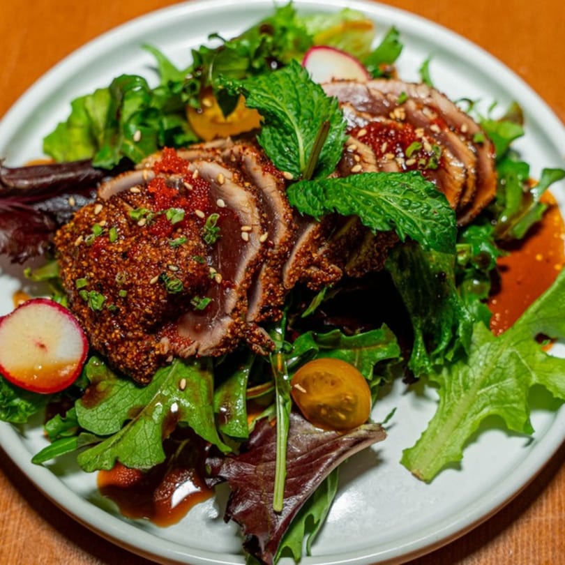 Seared tuna slices with sesame seeds, red roe, mint, and mixed greens on a white plate.